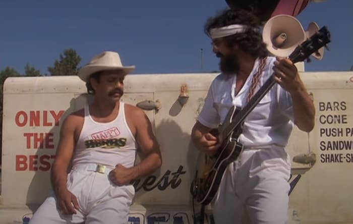 Cheech leans against a truck while Chong plays guitar