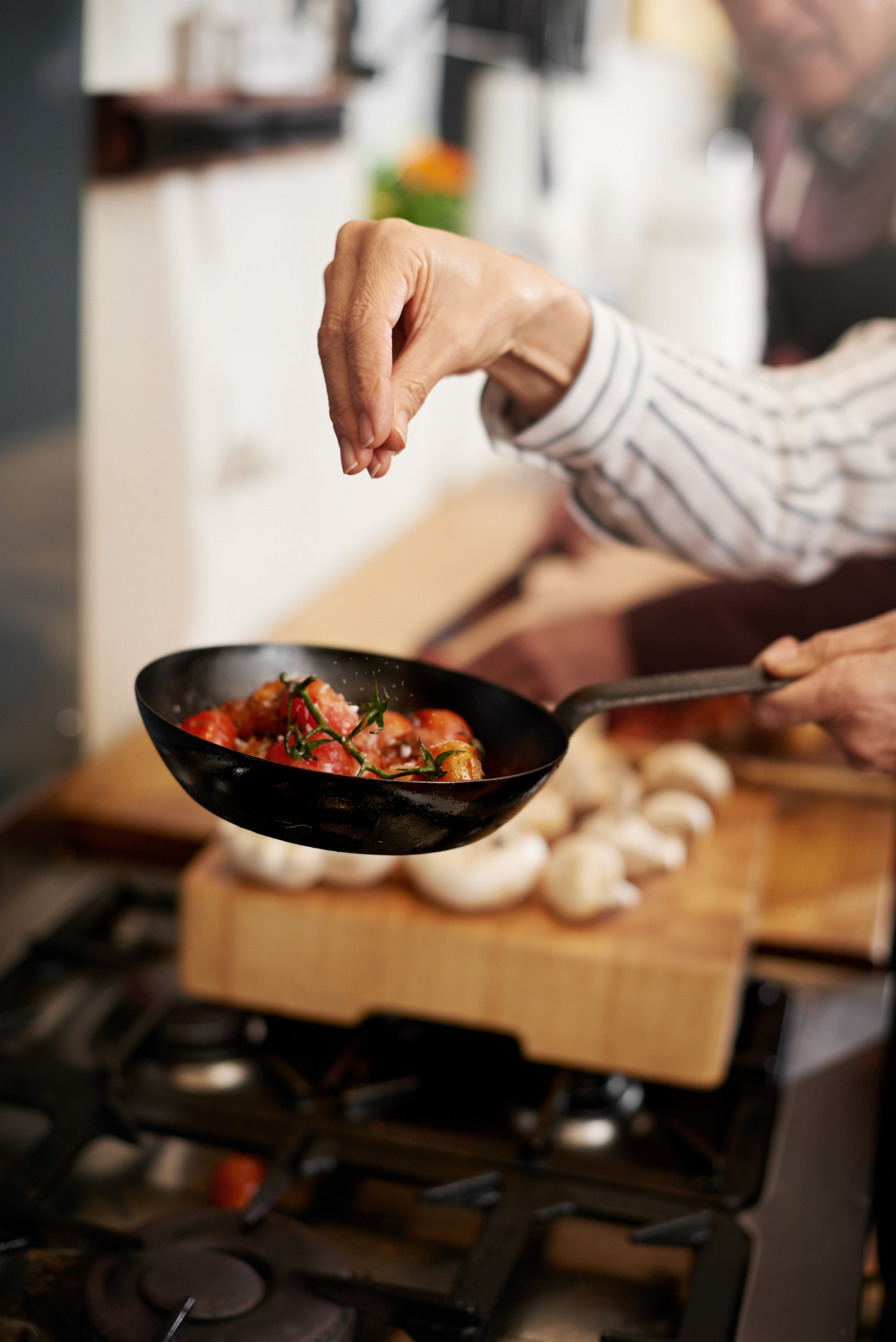 Cropped shot of a person&#x27;s hand adding salt to a pan of tomatoes in the kitchen