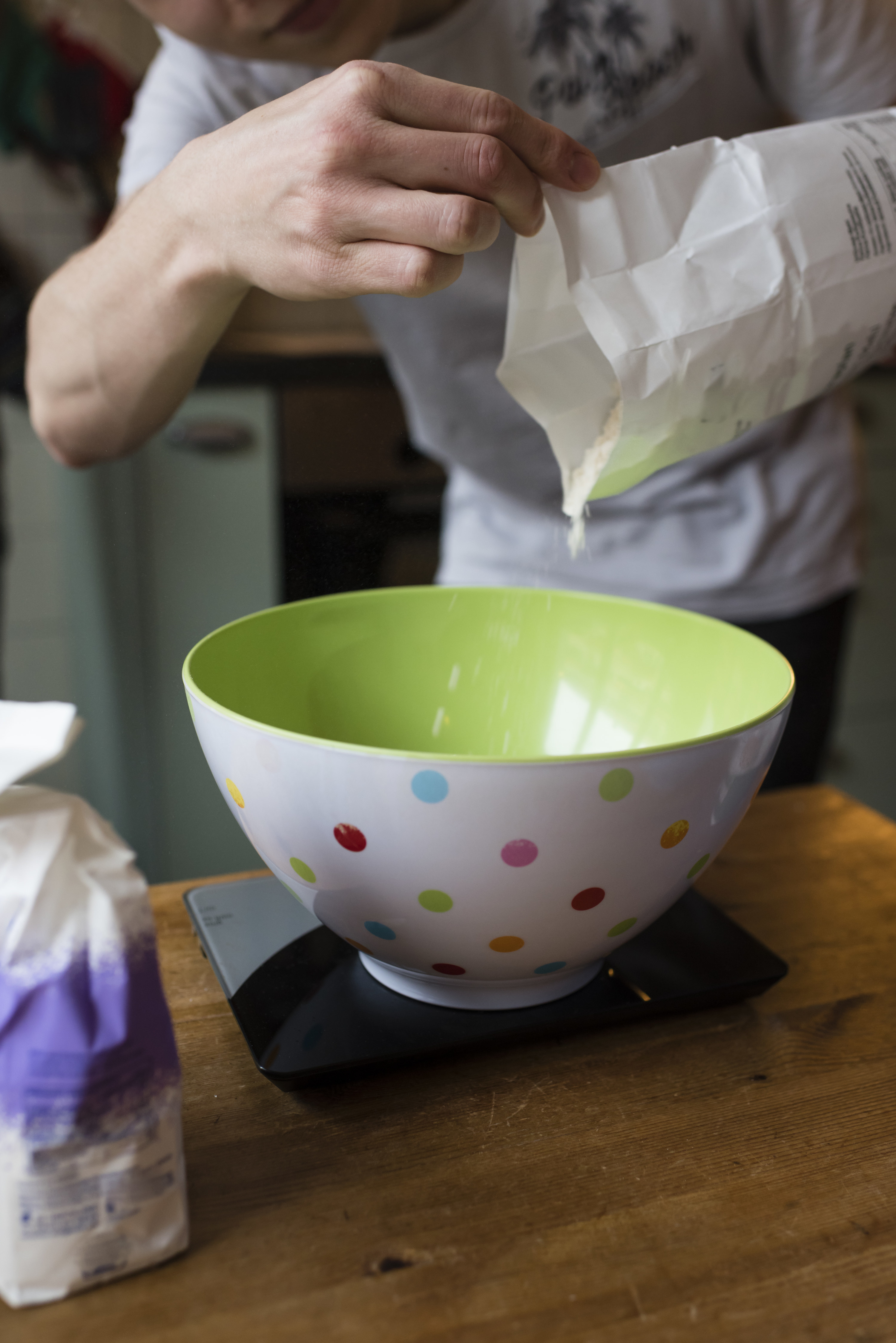 Weighing flour and adding it from a paper bag to a bowl to prepare the cookie dough.