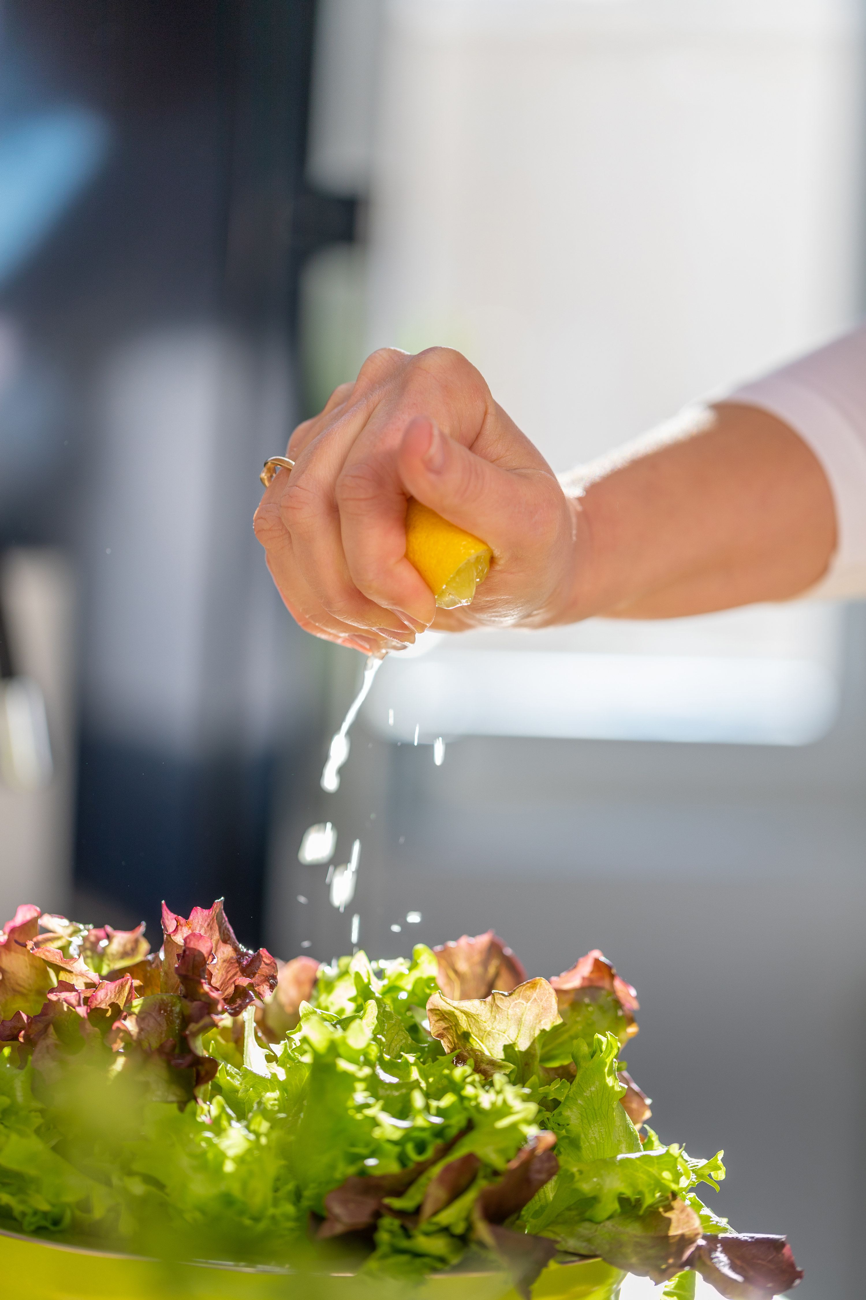 Close-up of female hand squeezing lemon juice on salad in a bowl