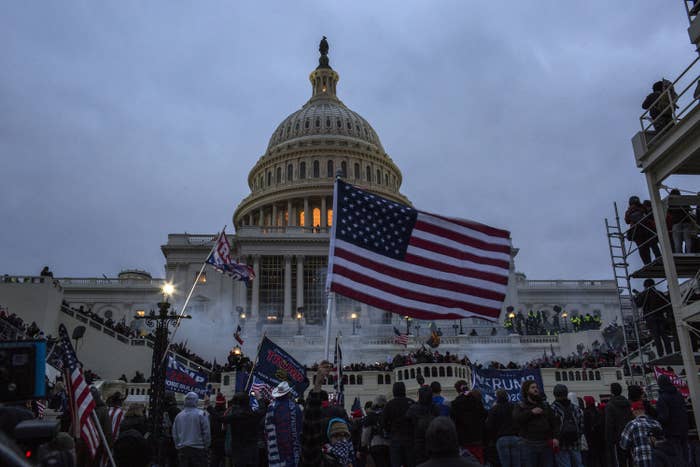 Tear gas surrounds rioters waving American flags in front of the US Capitol at night