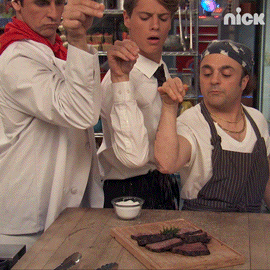 A GIF of three people sprinkling salt over steak on a cutting board