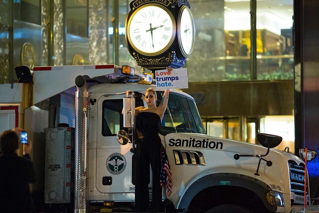 Lady Gaga standing on a dump truck and holding a sign that says &quot;Love trumps hate&quot;