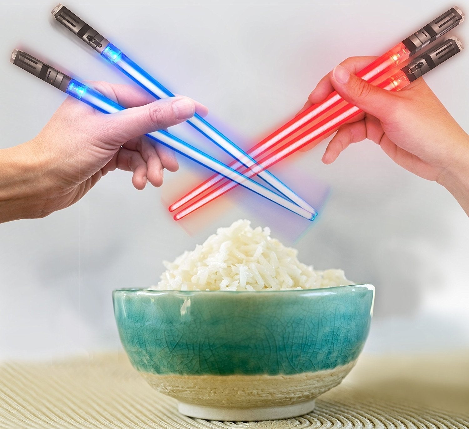 Two handles holding a pair of blue and red chopsticks that look like lightsabers over a bowl of rice 