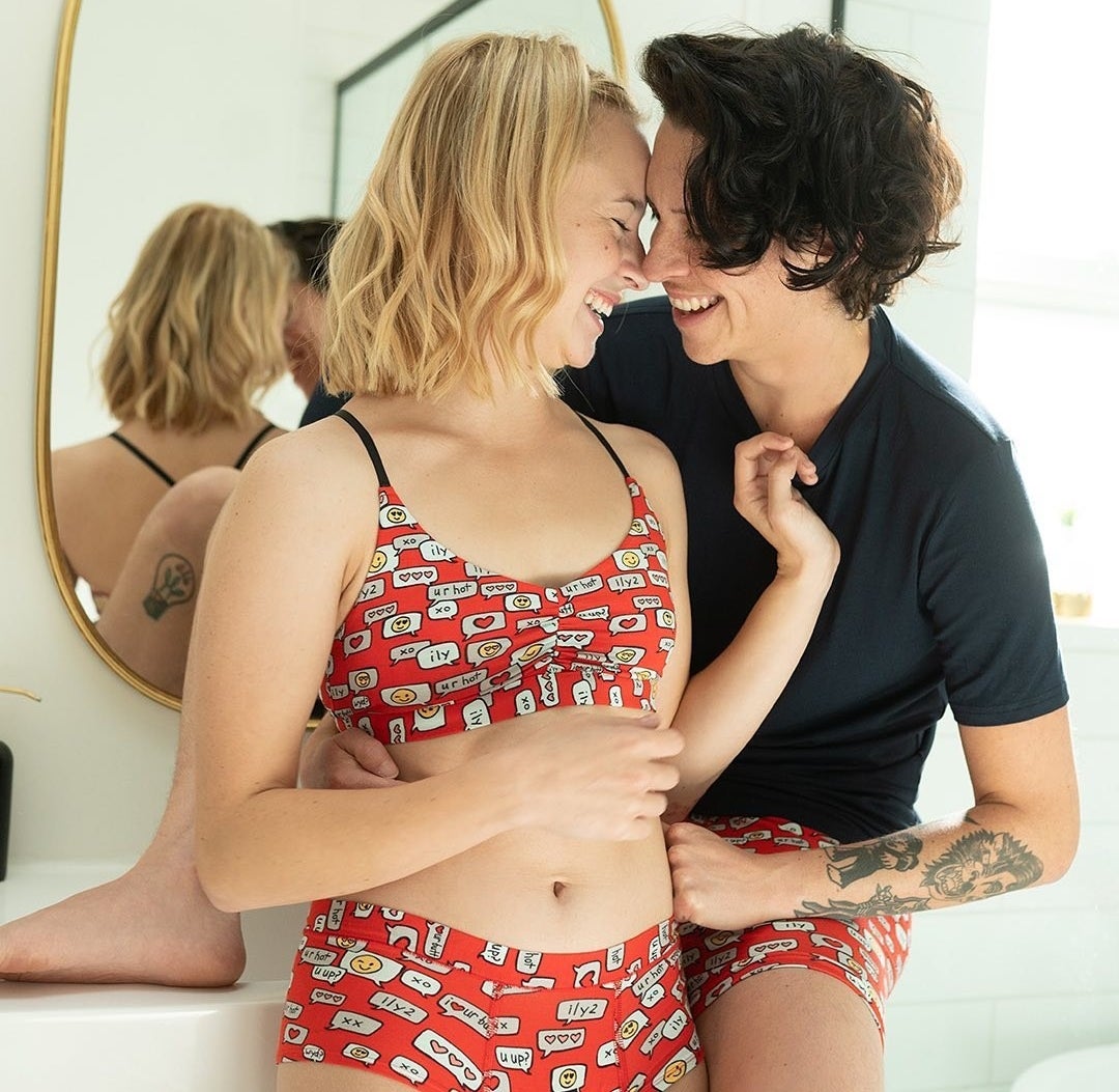 Two model wearing matching red underwear with illustrations of hearts and love-themed text messages