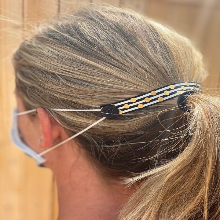 A model with a decorative fabric strip with buttons on either side of it wrapped around the back of their head to attach to the straps on a face mask 