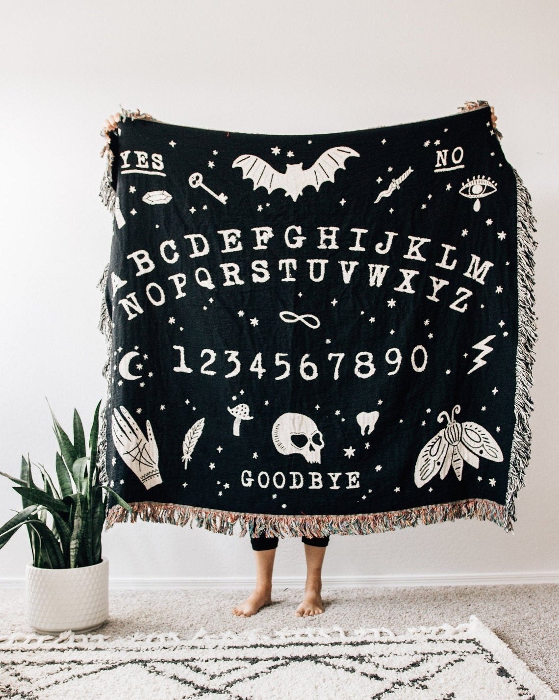 Black blanket with illustrated ouija board and tassels on edges 