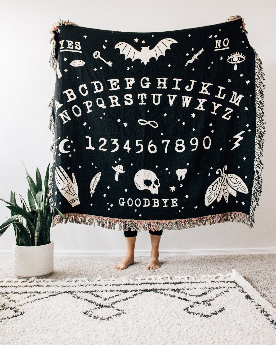 Black blanket with illustrated ouija board and tassels on edges