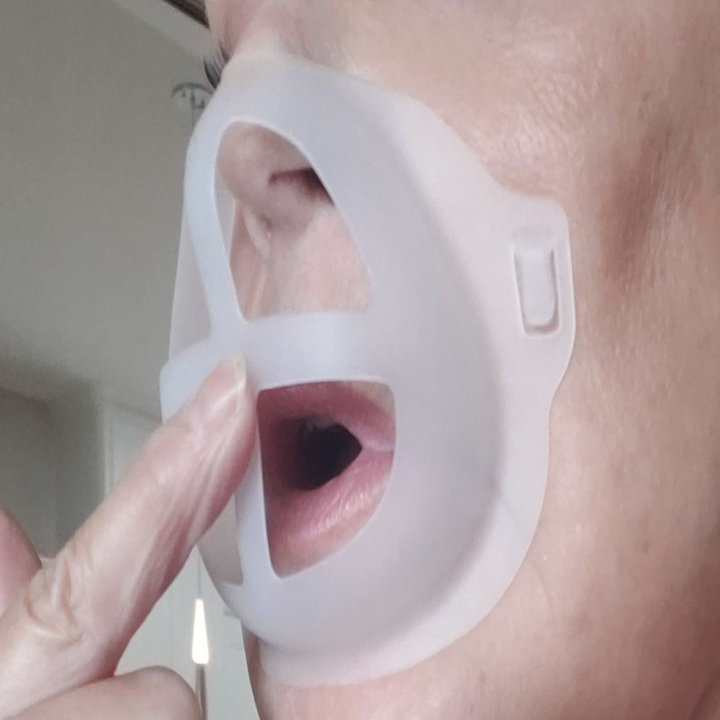 Reviewer holding up transparent silicone dome-shaped mouth guard over their lips 