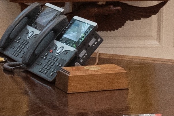 The red button inlayed in wood laid next to two landline phones