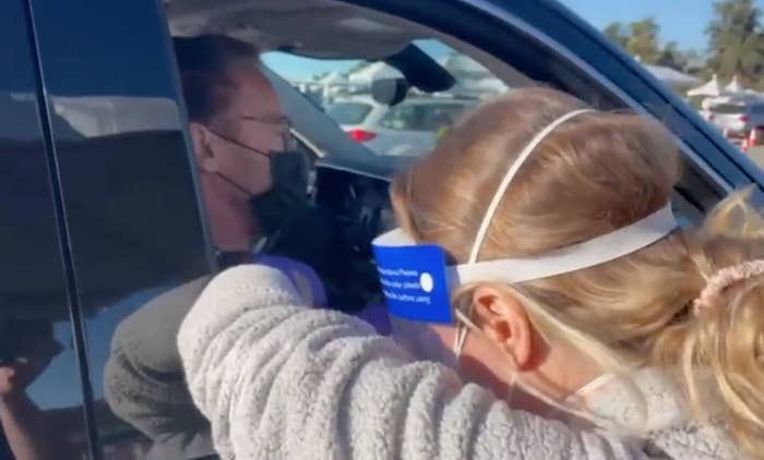 An essential healthcare worker reachers through the passenger's window of the vehicle to administer Arnold's shot
