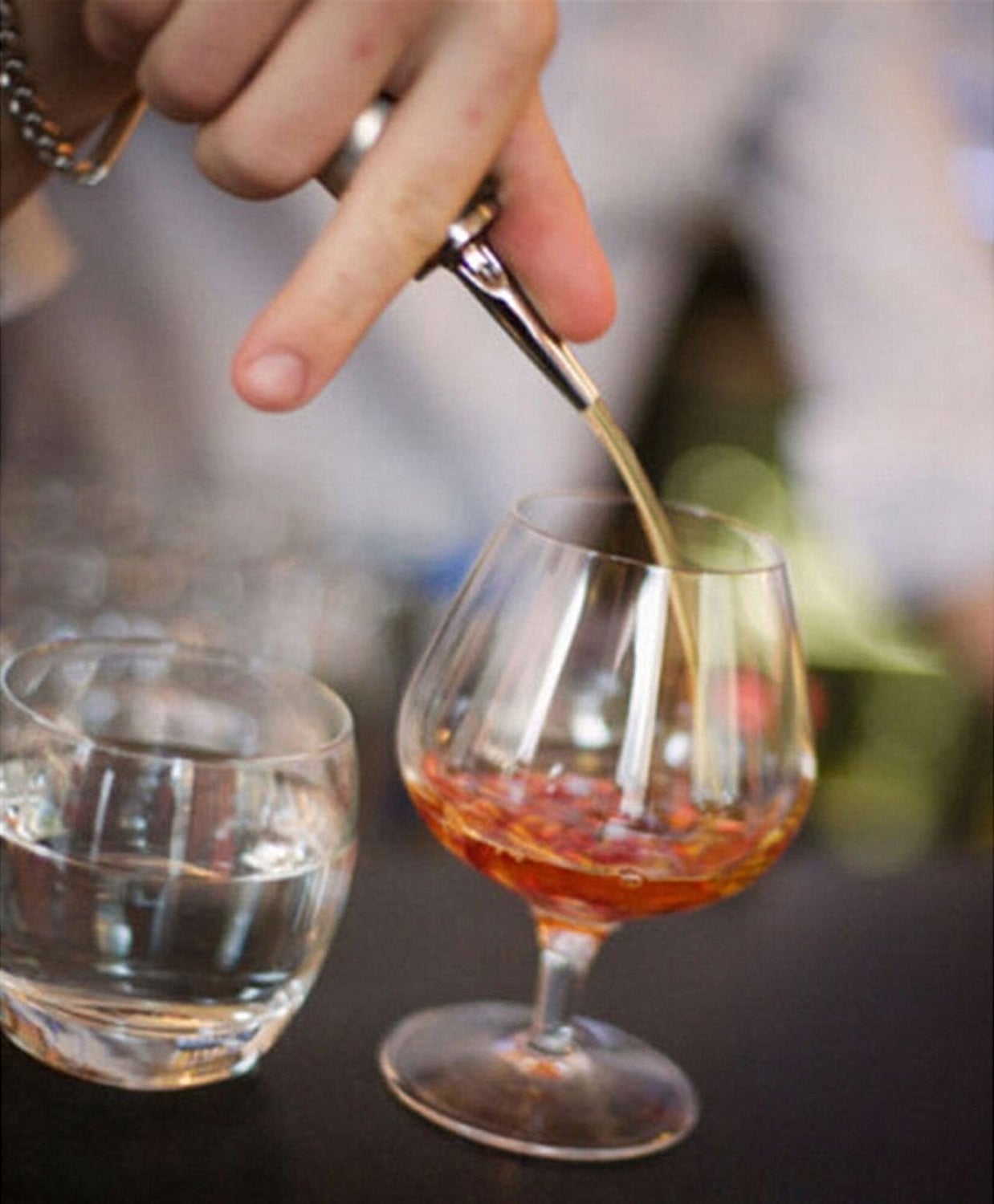 A person pouring a drink with the metal pourer attached to the bottle.