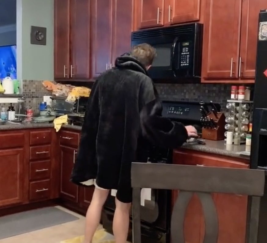 The boyfriend stands in the kitchen in a snuggie
