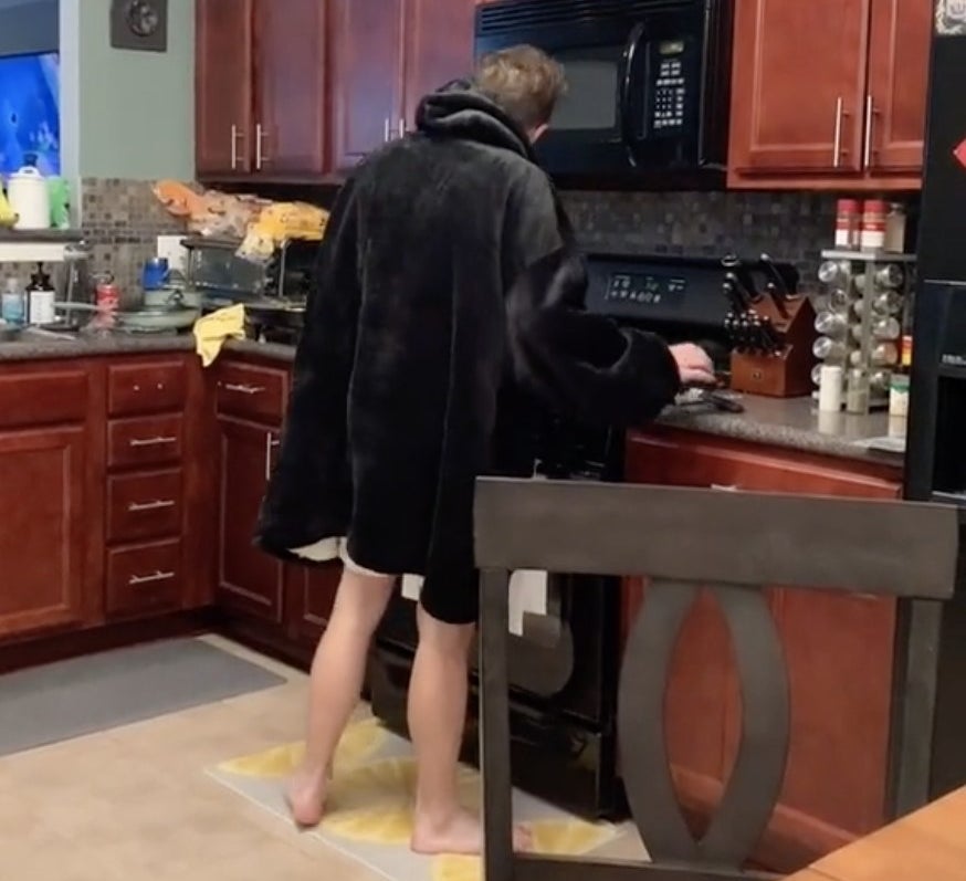 The boyfriend stands in the kitchen in a snuggie