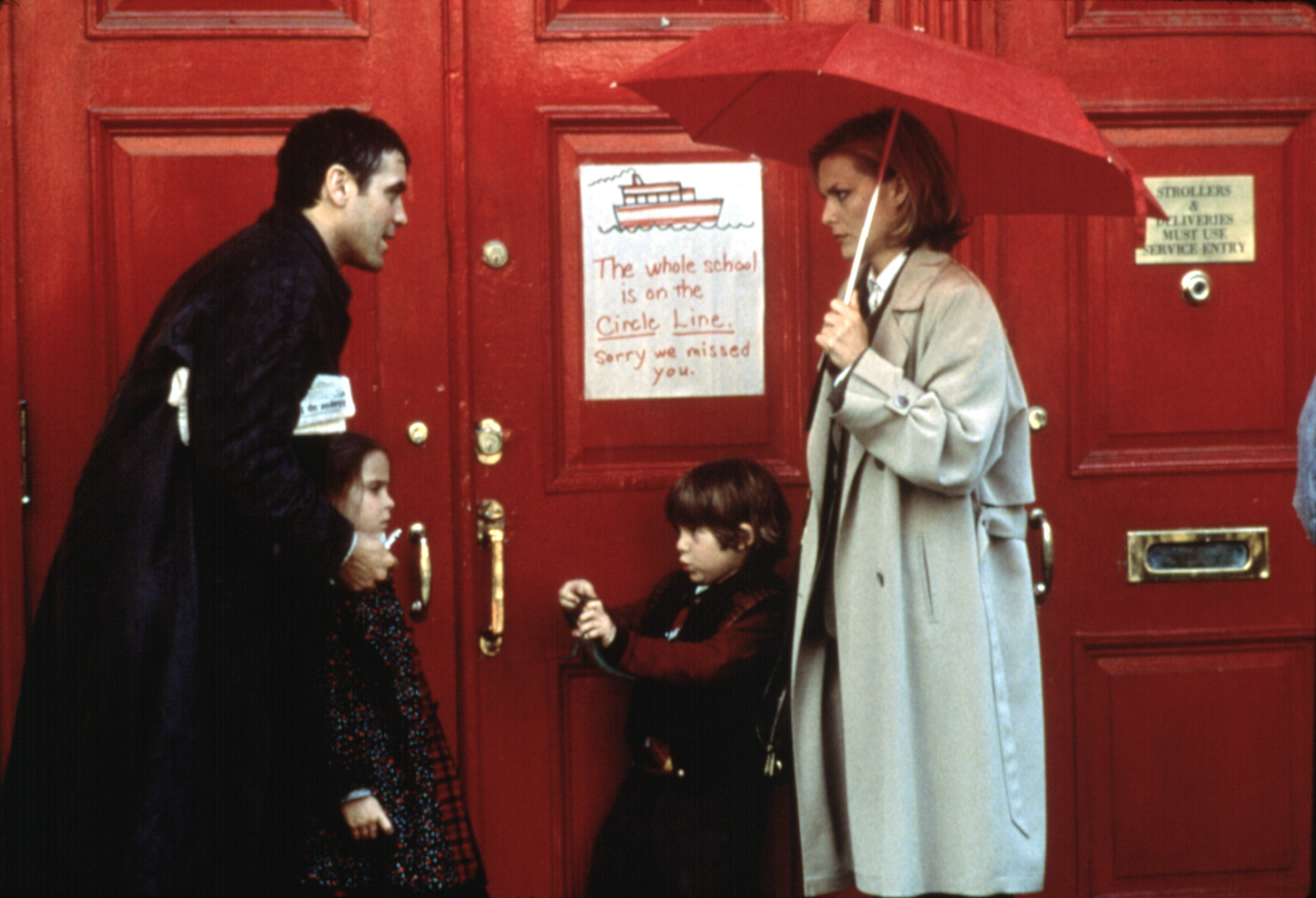 George Clooney, Mae Whitman, Alex D. Linz, Michelle Pfeiffer standing in the rain outside of a building with a sign that says &quot;The whole school is on the Circle Line, Sorry We Missed You&quot;