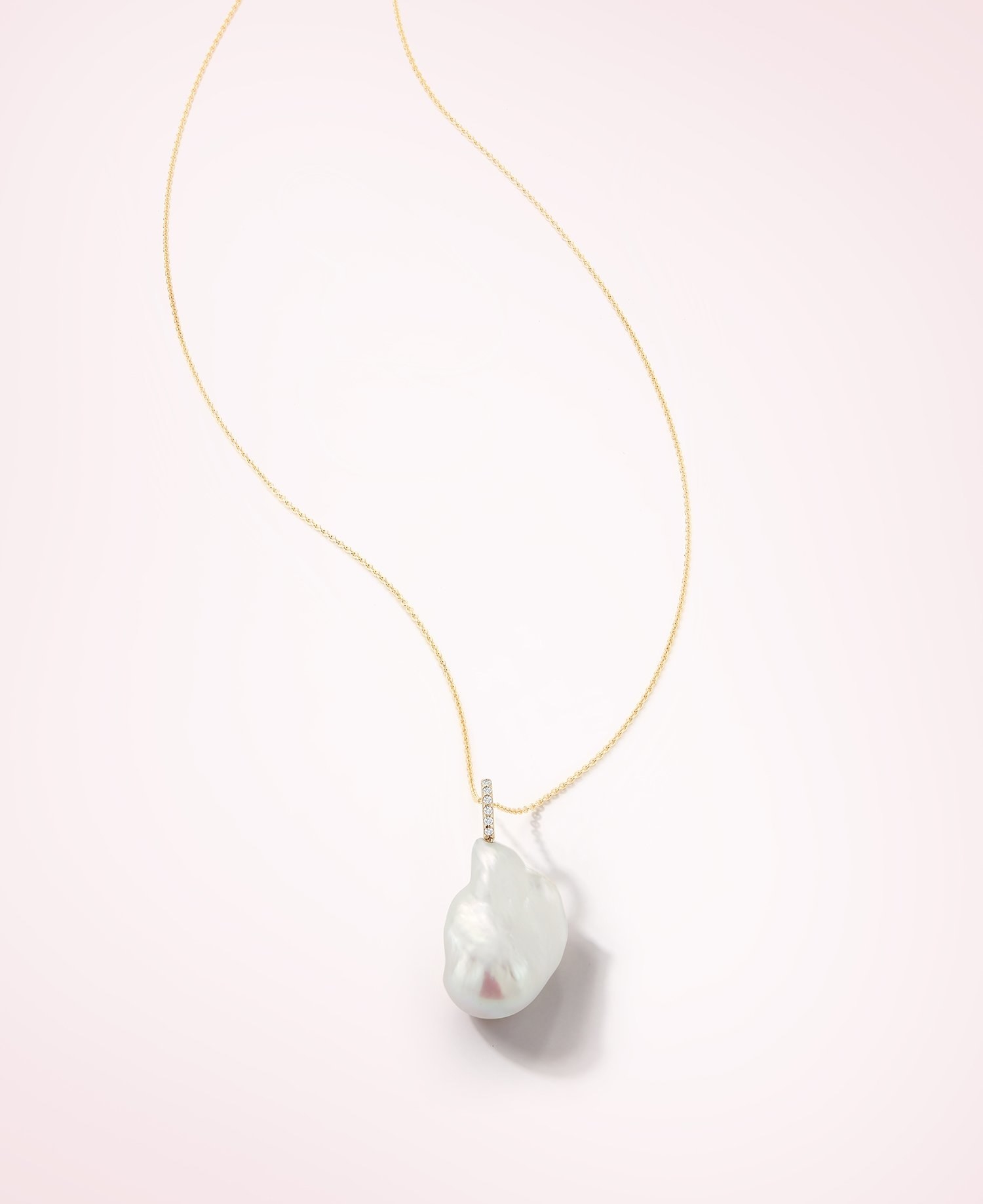 A gold chain with a baroque pearl hanging from a diamond line