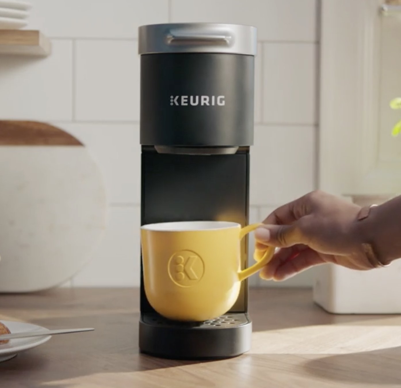 Person is placing a yellow mug on a black Keurig mini coffee maker
