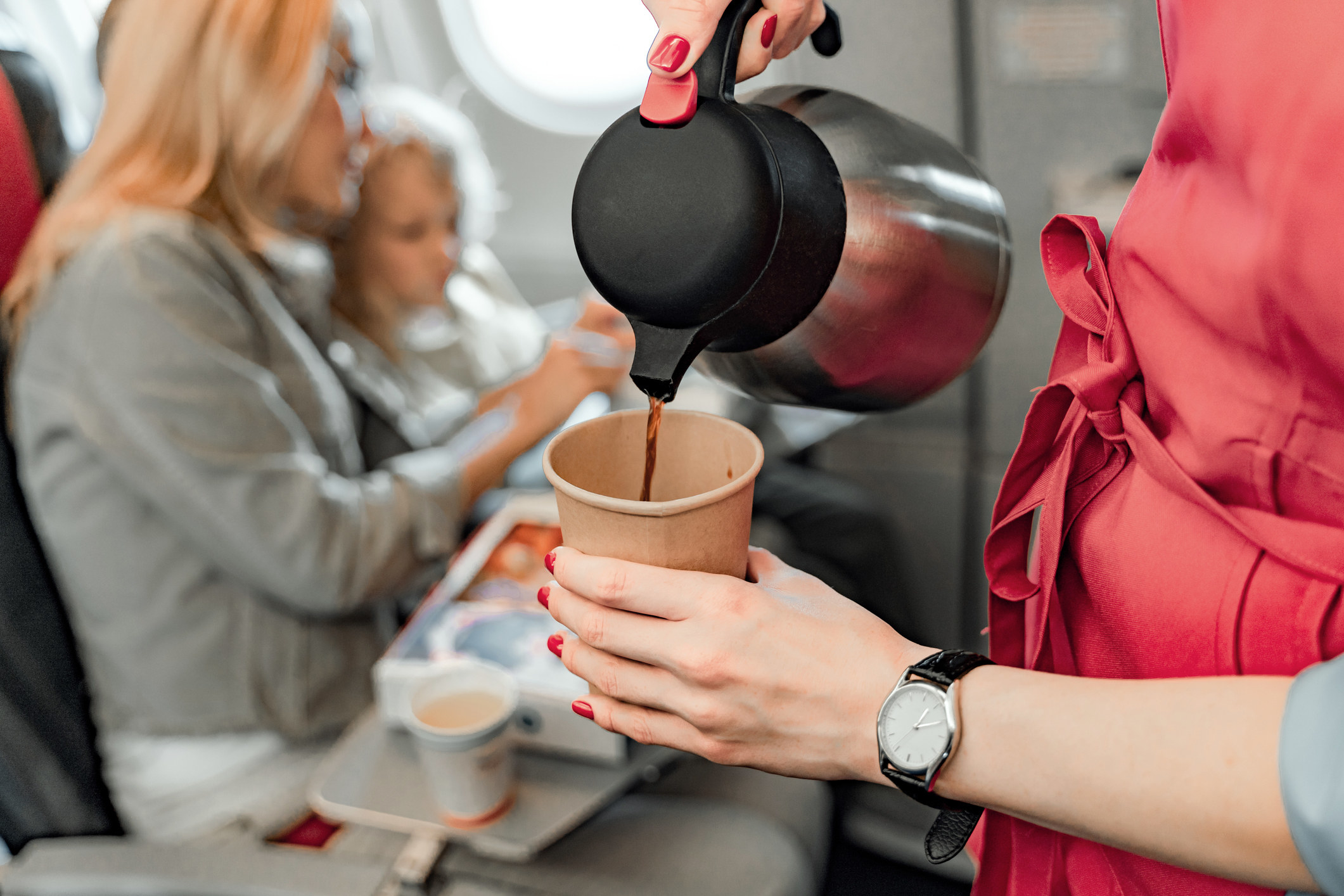 A flight attendant pouring coffee next to a woman and a child