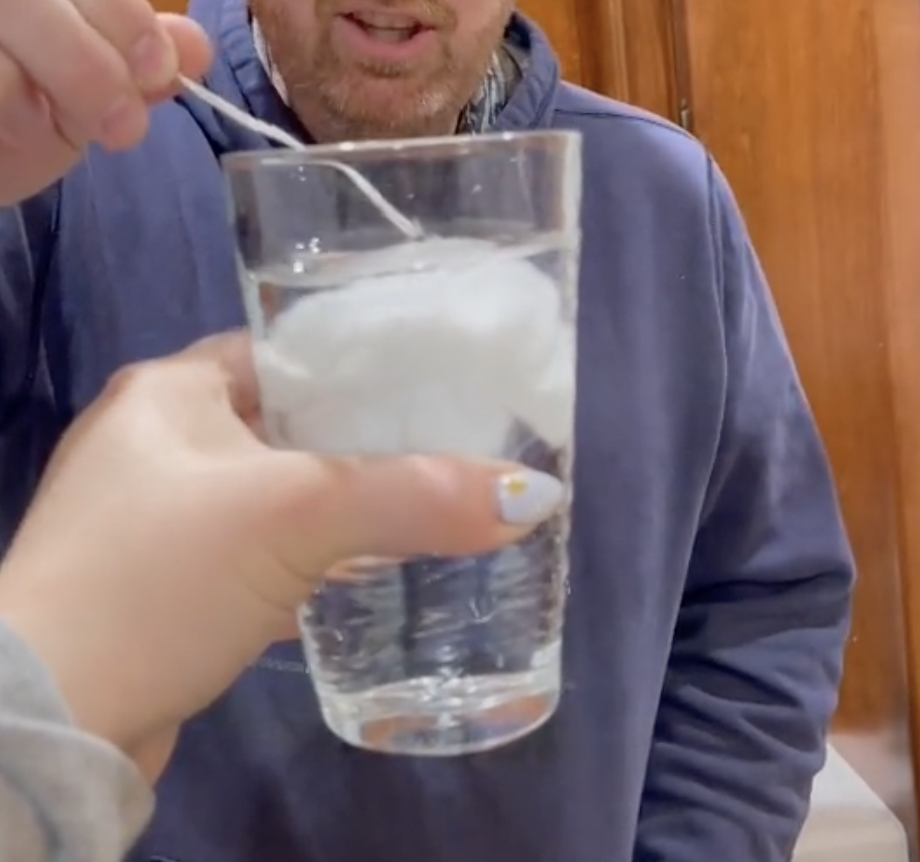 A man looking at an expanded tampon inside a glass filled with water