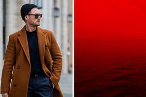 A man walks down the street wearing a beanie and sunglasses and a red hued fog falls over a body of water.
