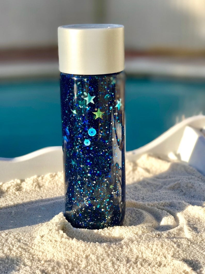the dark blue sensory bottle with sequins in the sand 