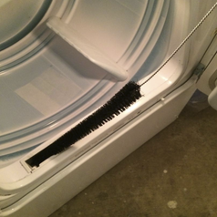 the dryer vent brush which is long and skinny with bristles being held by a reviewer over the vent where the filter slides in