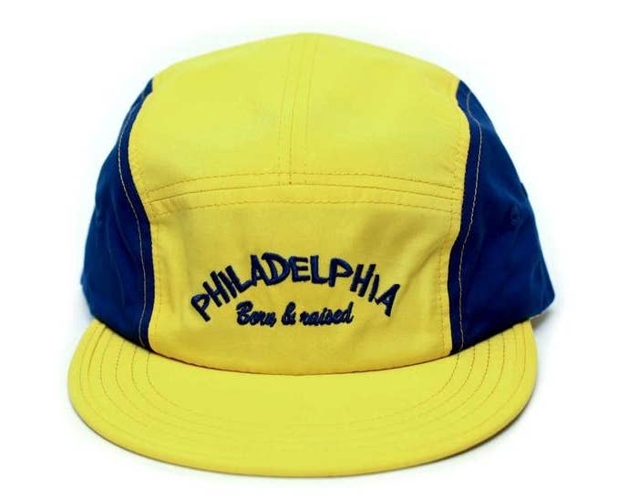 yellow and blue baseball-style cap that says "Philadelphia born and raised" on the front