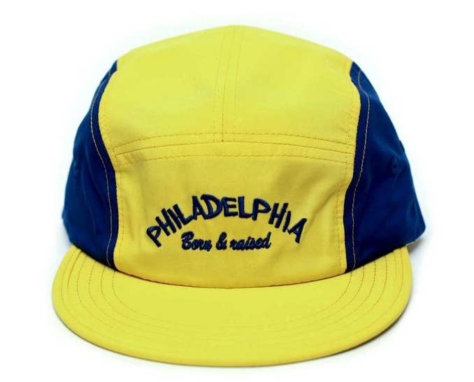 yellow and blue baseball-style cap that says &quot;Philadelphia born and raised&quot; on the front 