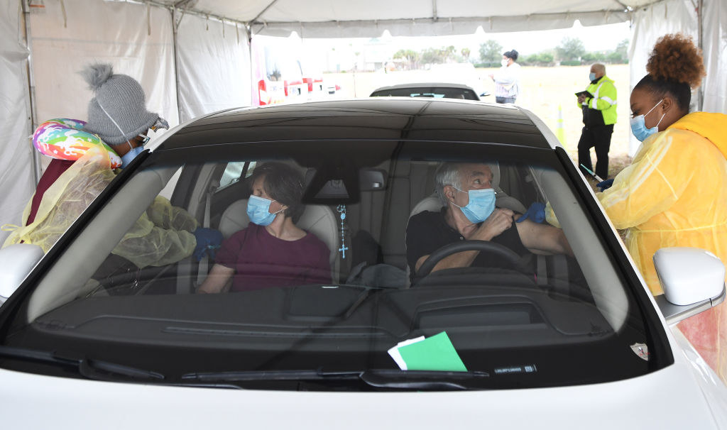 Two older people receive COVID-19 shots while seated in their car. 