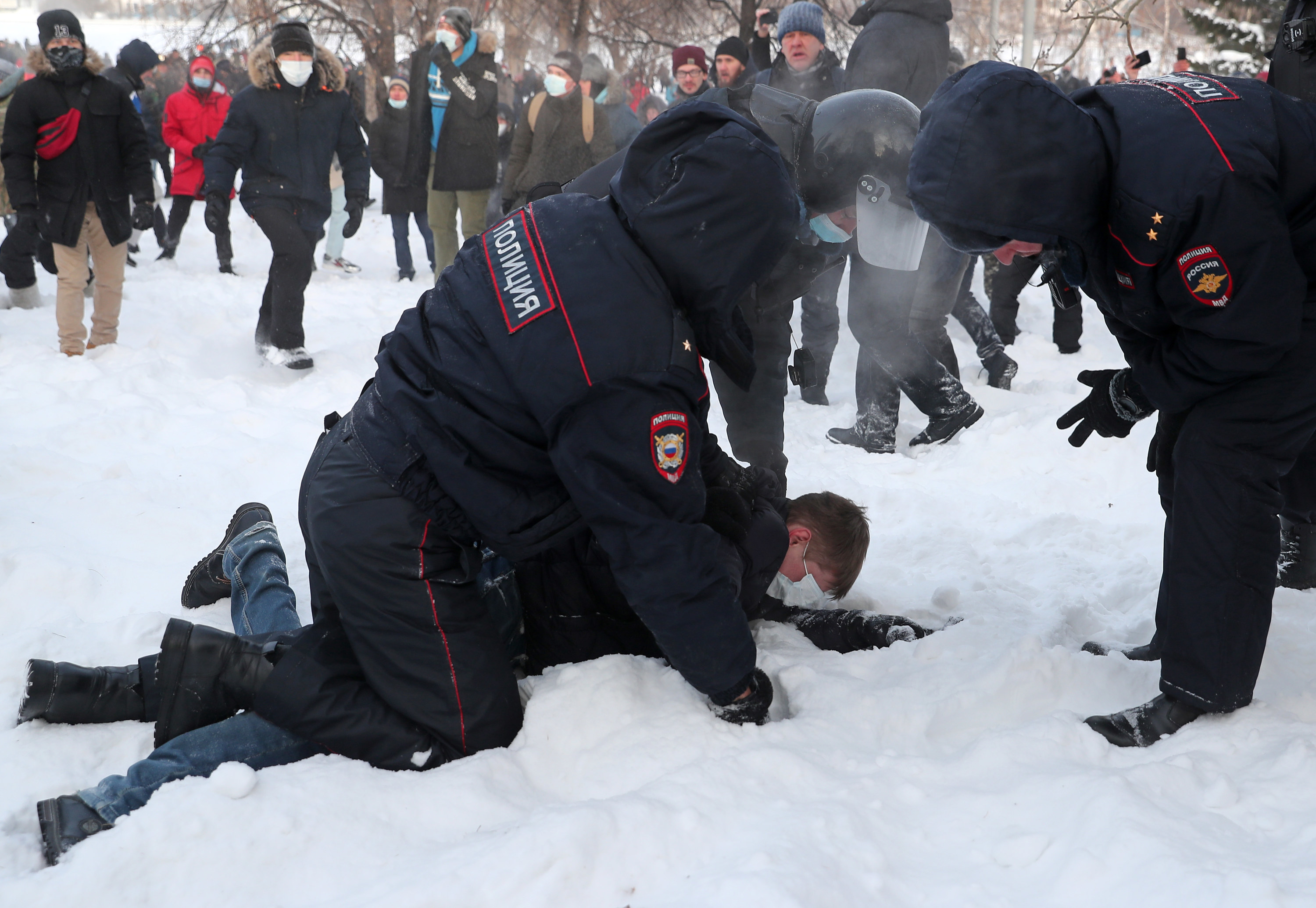 Police officers in uniform hold a man wearing a face mask down on the ground in the snow