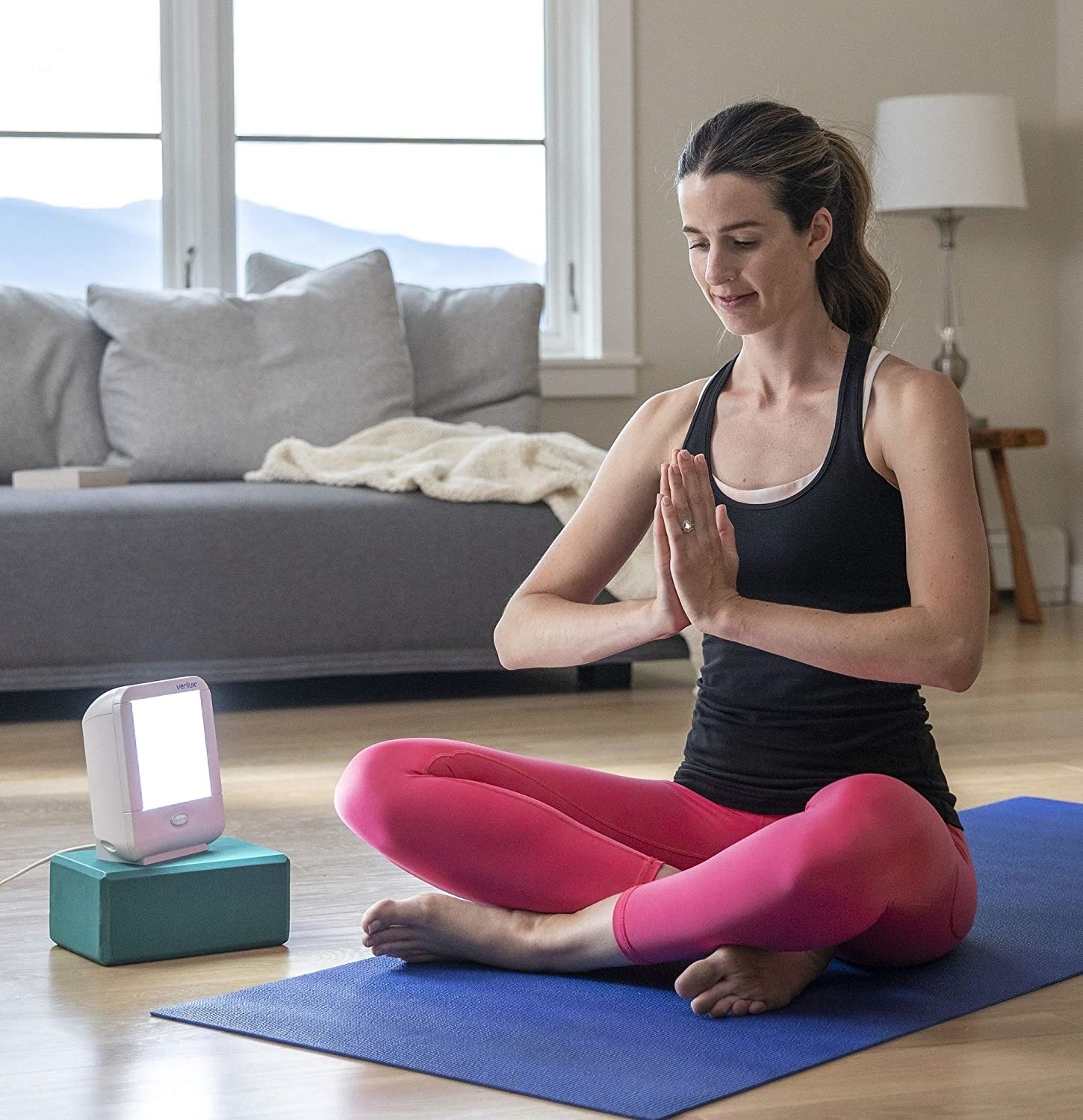 A person sitting crossed legged on a yoga mat with a small lamp beside them