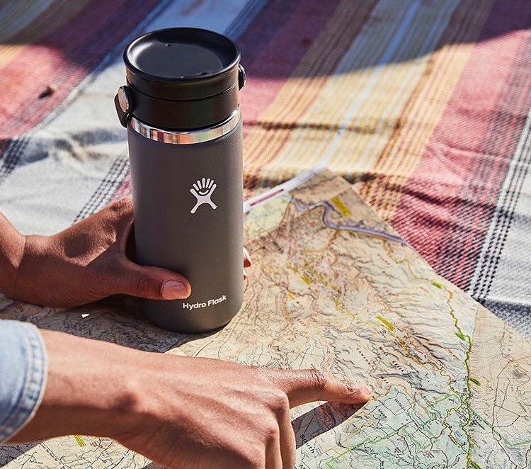 A person holding a travel coffee mug while looking a map