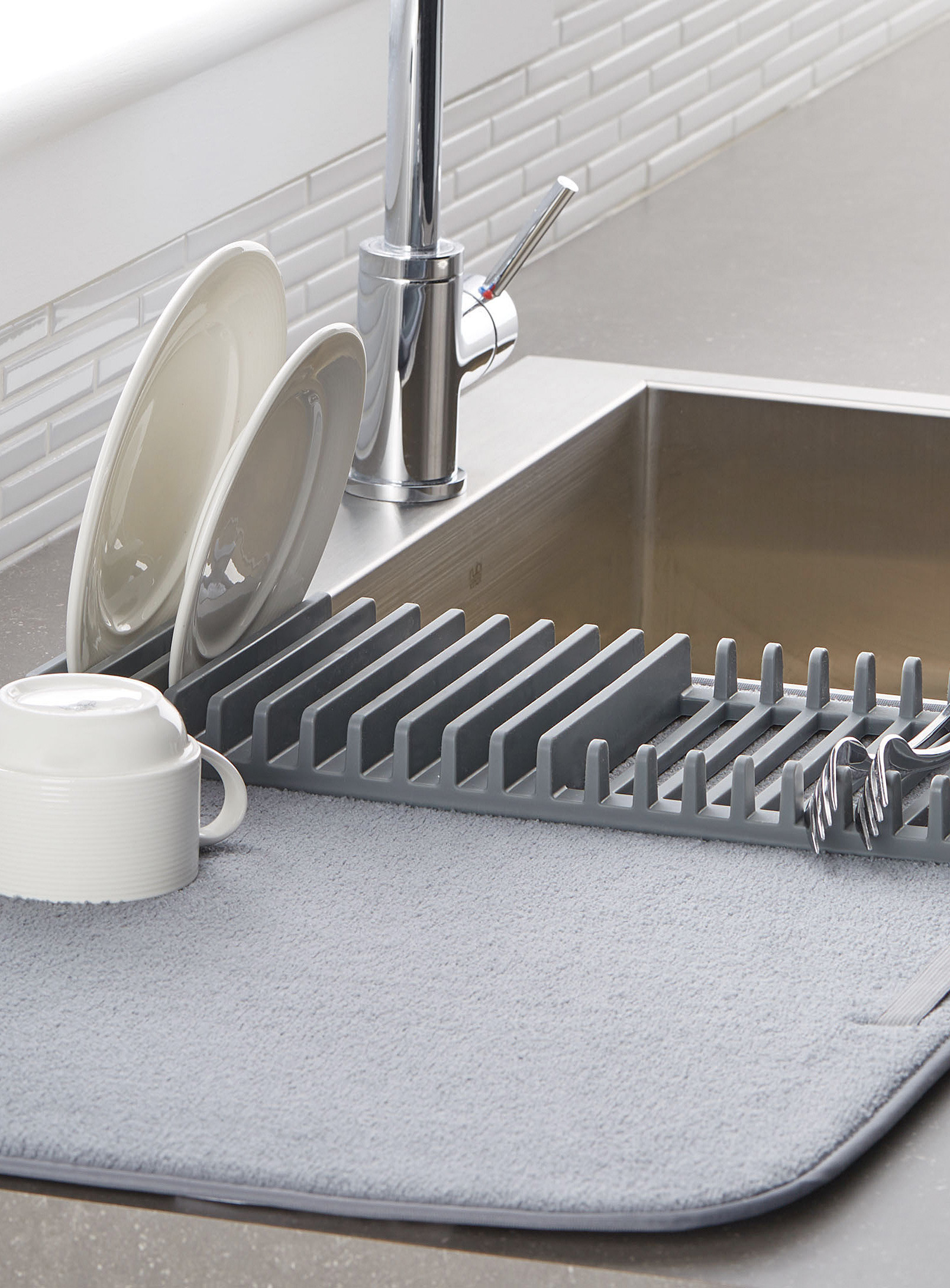 A silicone dish rack attached to a large micofibre mat that has a cup, plates and a couple of forks drying on it