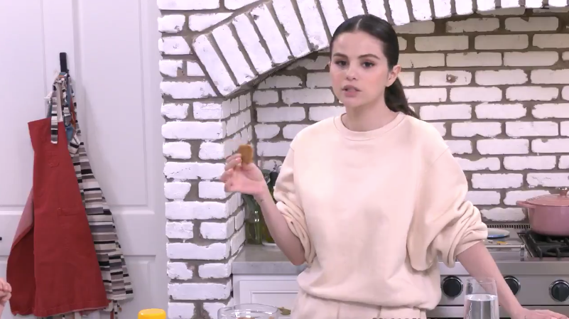 Selena in her kitchen, holding up an ANZAC biscuit 