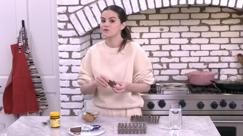 Selena in her kitchen, holding up a Tim Tam