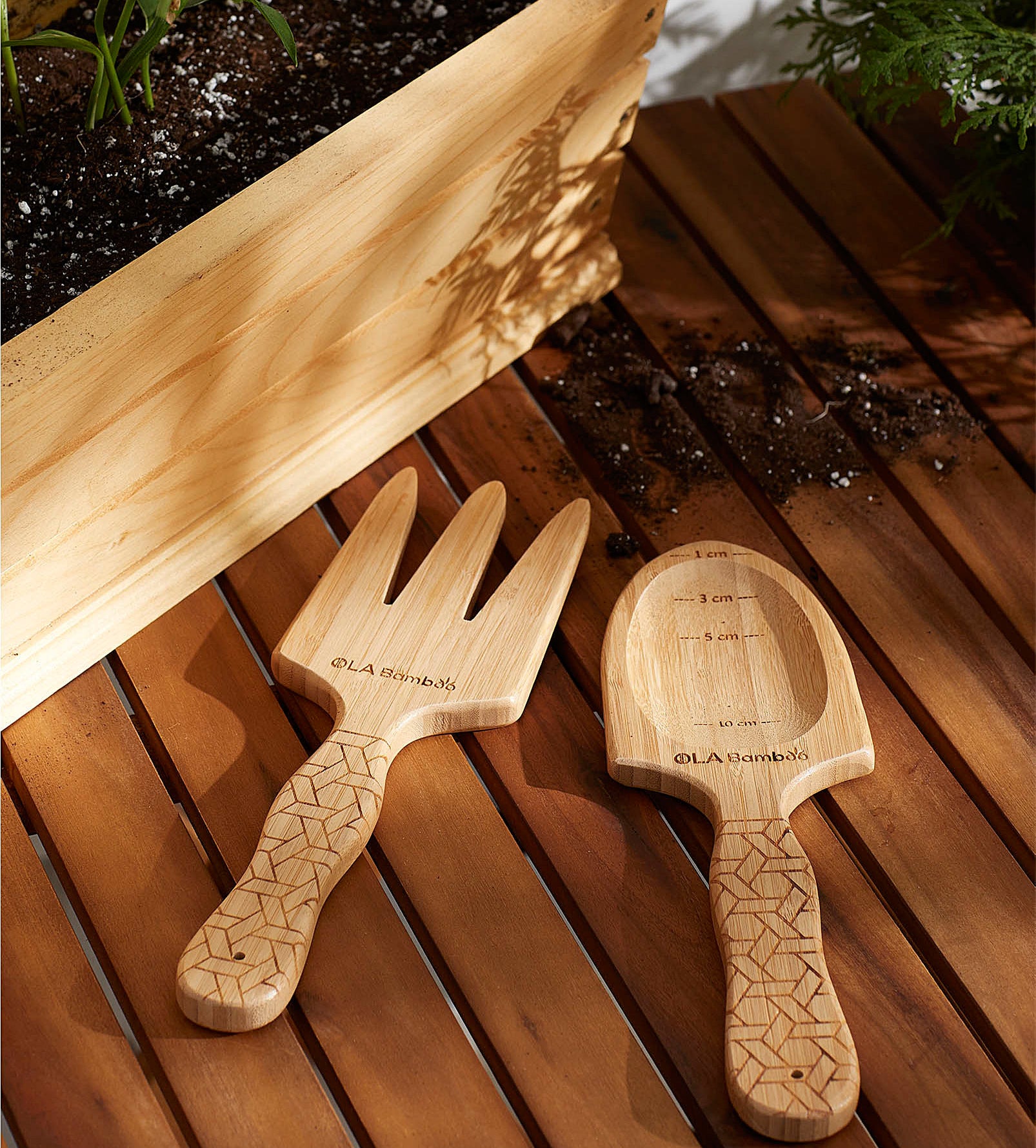 A wooden rake and spade next to a small flower bed