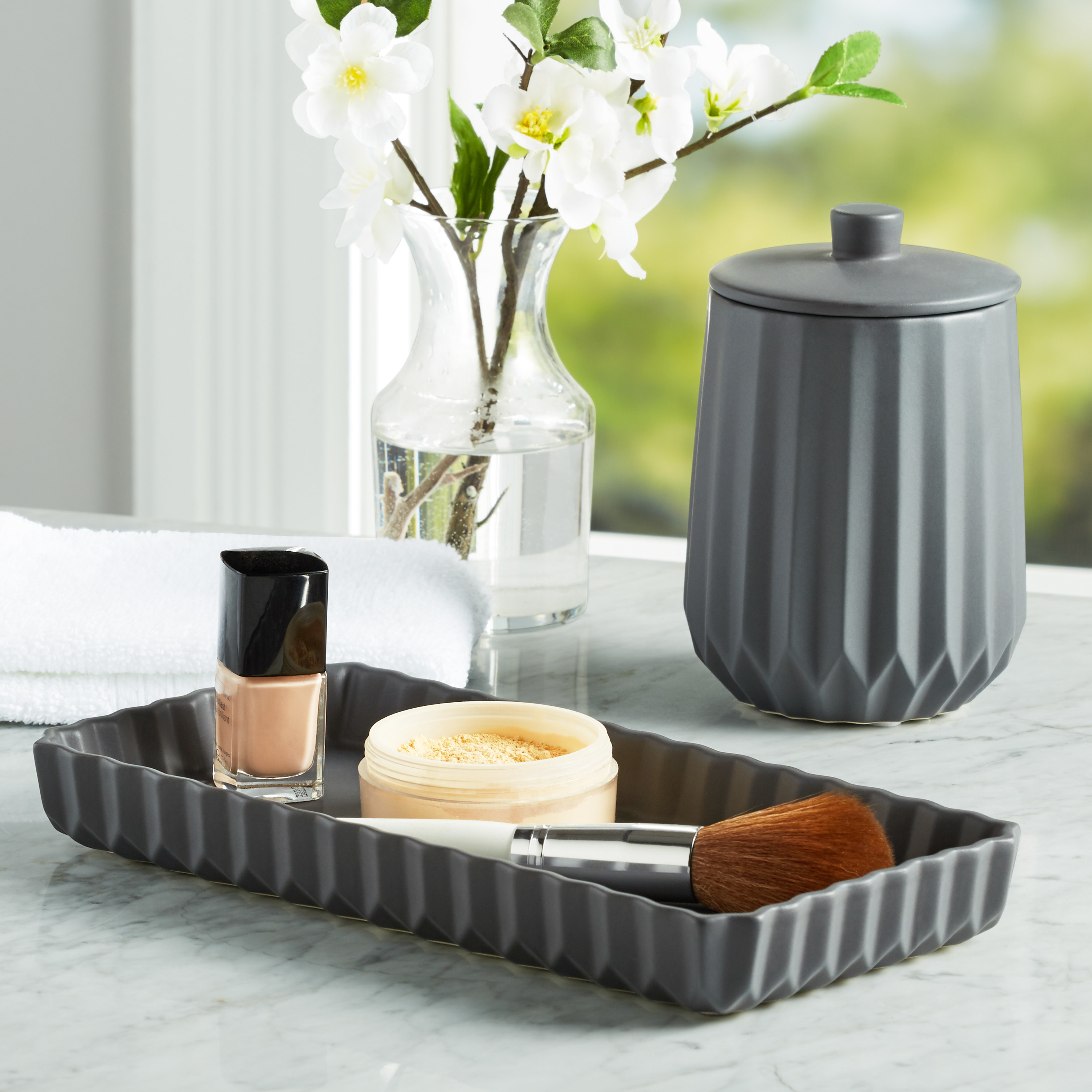 A grey tray holding cosmetics and a great jar with lid