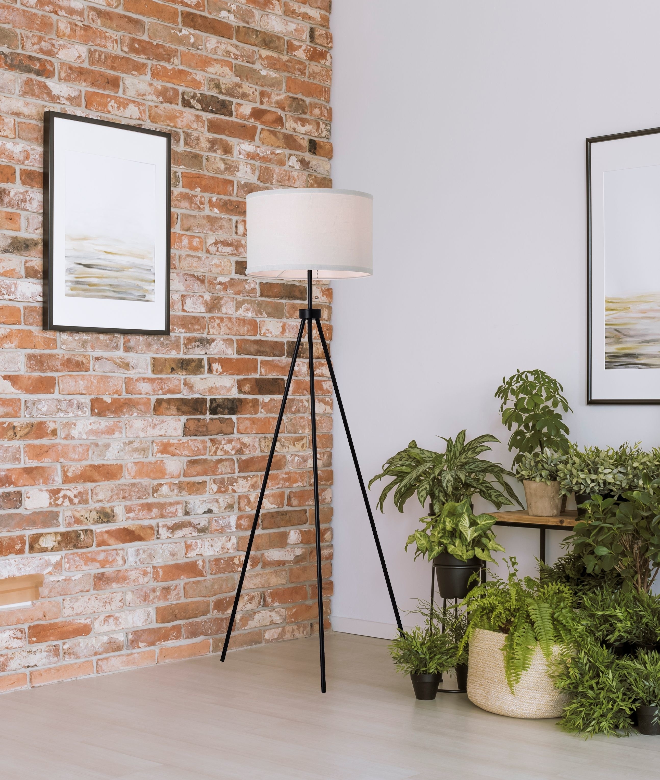 a black metal tripod lamp with a white lampshade in a corner