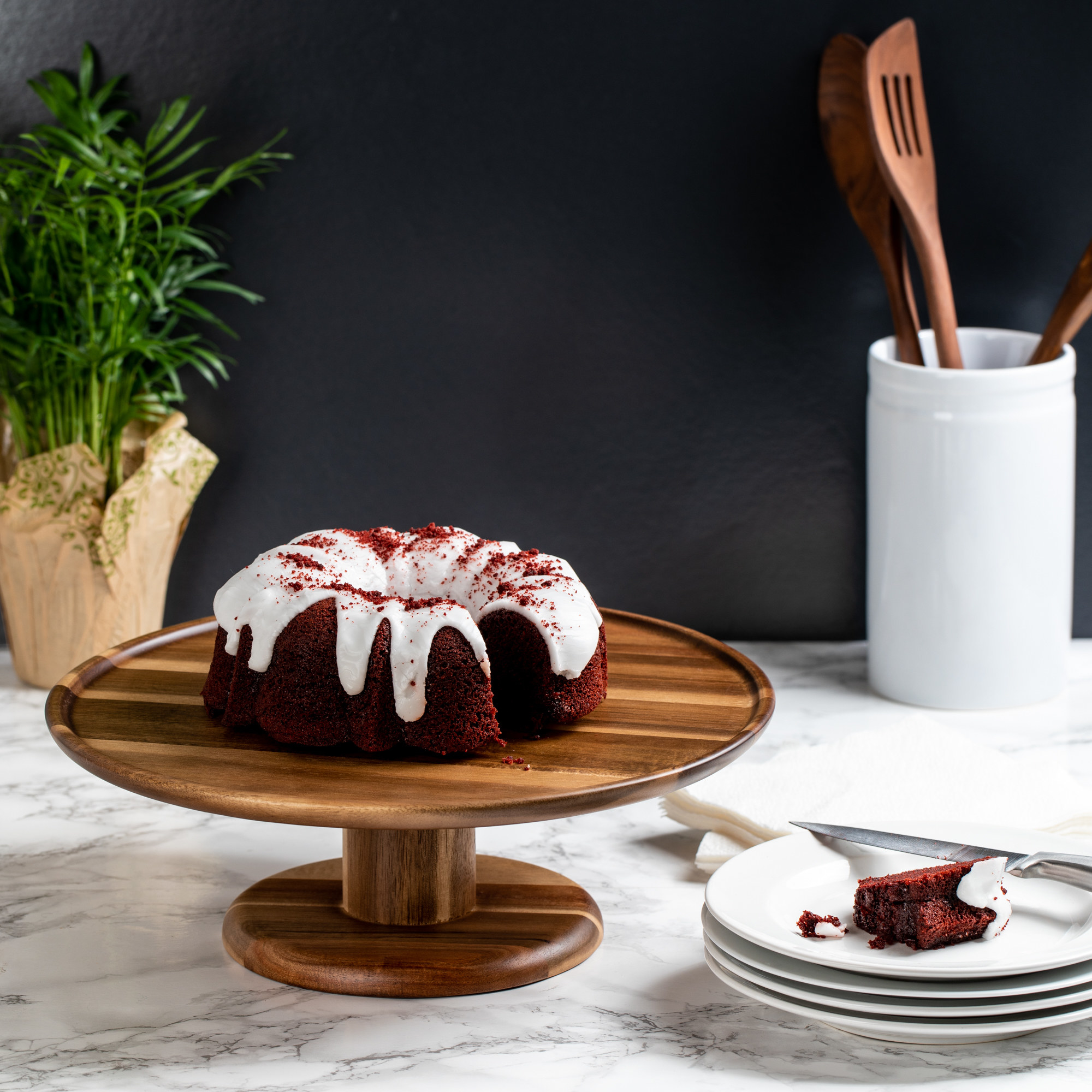 an acacia wood cake stand holding a bundt cake on a counter