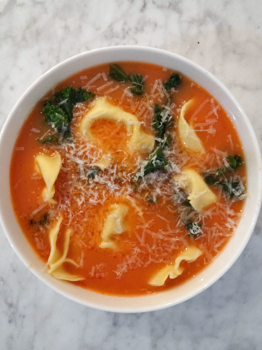 A bowl of tomato soup with tortellini and kale.