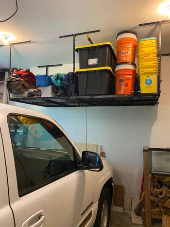 A reviewer's photo of the black shelving unit holding various buckets, storage containers, and camping equipment