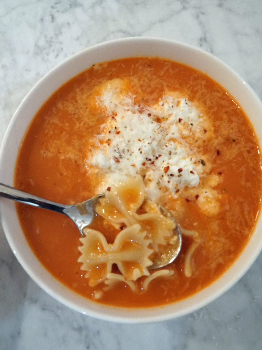A bowl of tomato lasagna soup with ricotta and bow tie pasta.