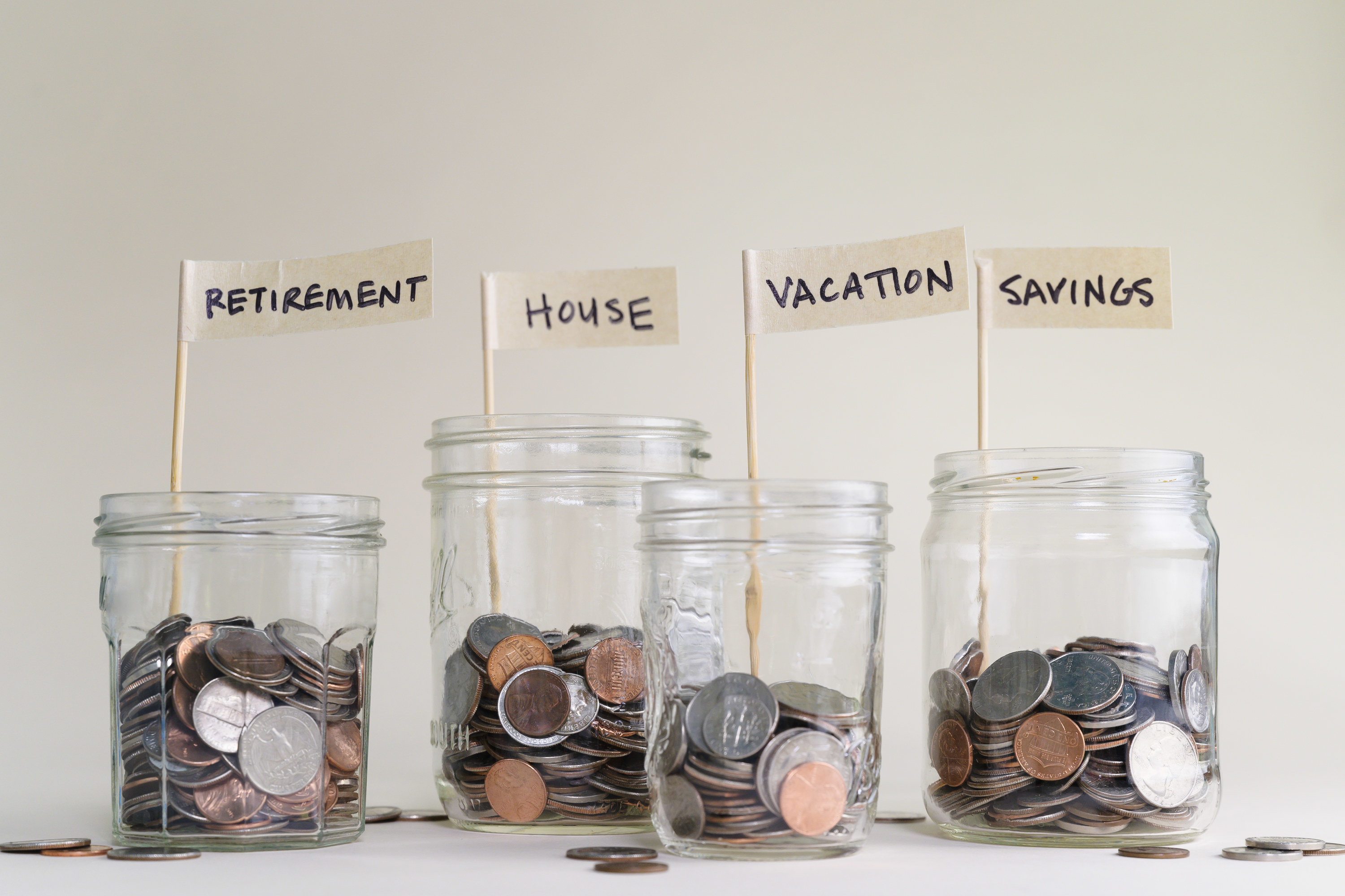 Jars of coins labeled with the savings categories: retirement, house, vacation, and savings