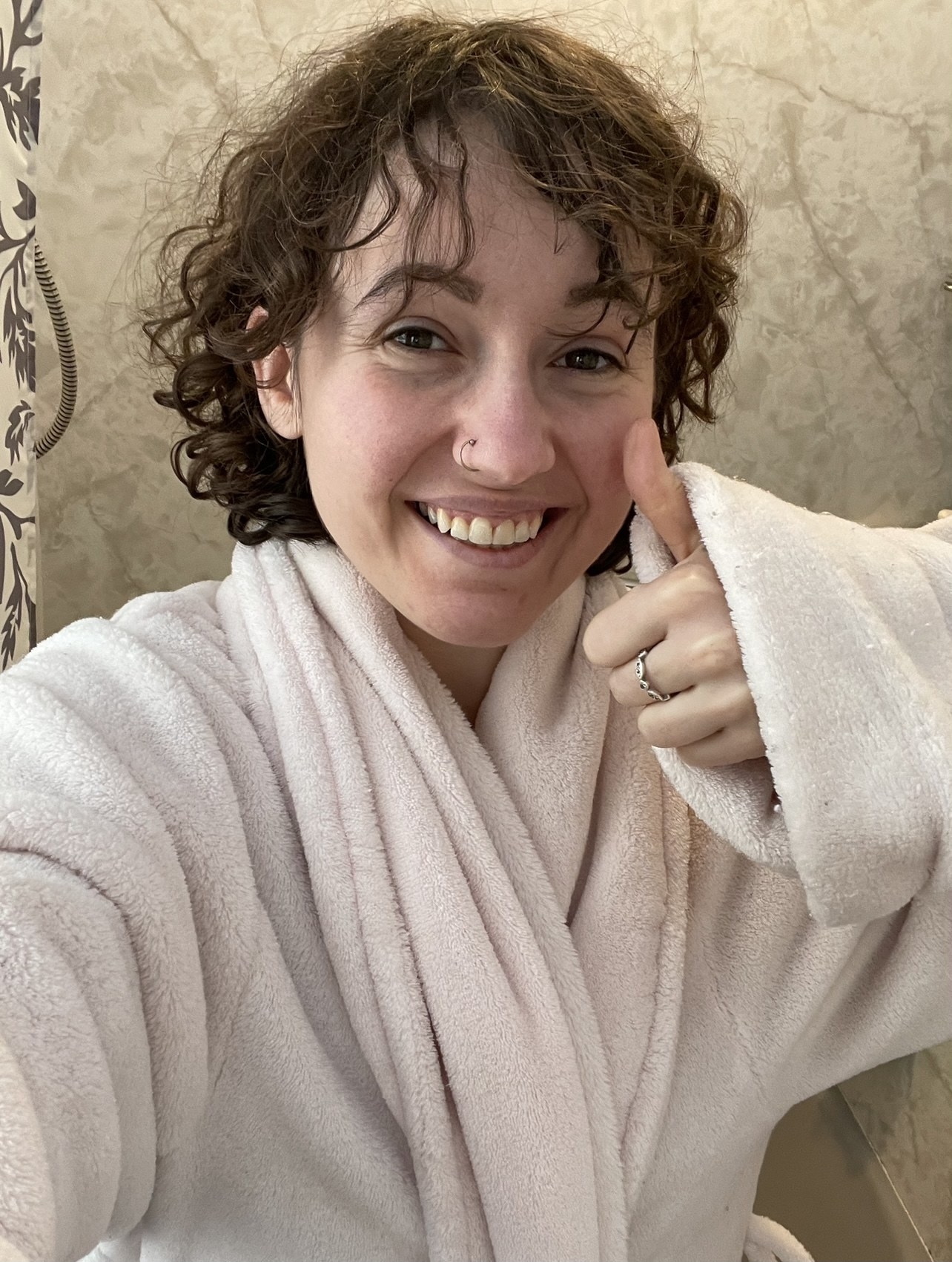 A person smiling with a thumbs-up in a pink bathrobe
