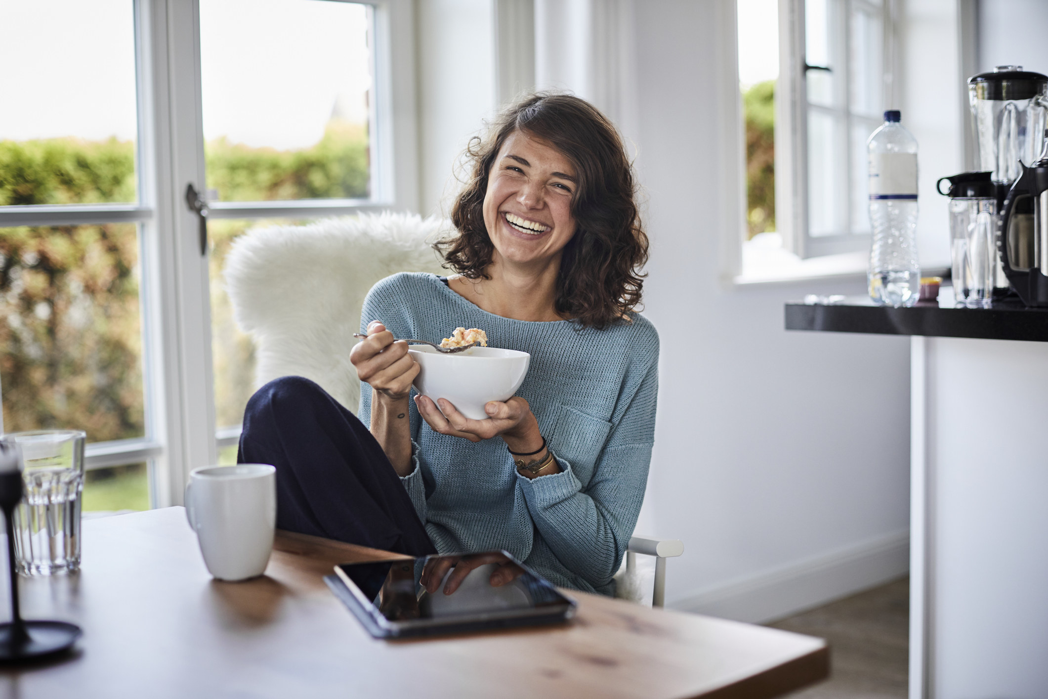 A young woman smiling eating a bowl of cereal.