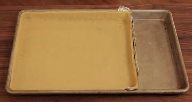 A tart shell covering about 80% of a sheet pan, which has been down-sized with a foil strip