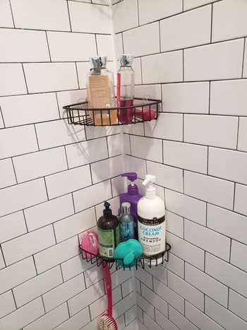 A reviewer's photo of the black caddies holding body wash, loofahs, and other bath products
