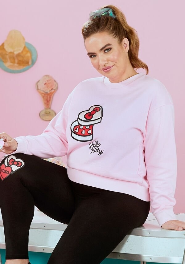 Model wears pink sweatshirt with Hello Kitty-themed box of chocolates and logo on front