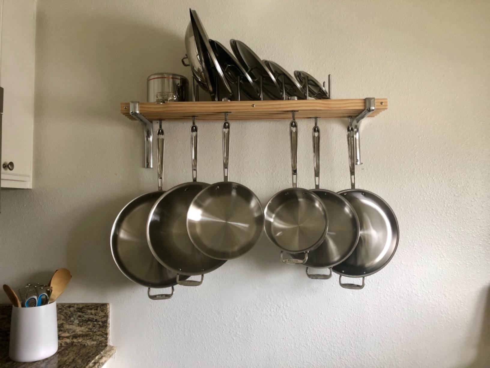 A reviewer&#x27;s photo of the rack holding six pans and their lids on the top shelf