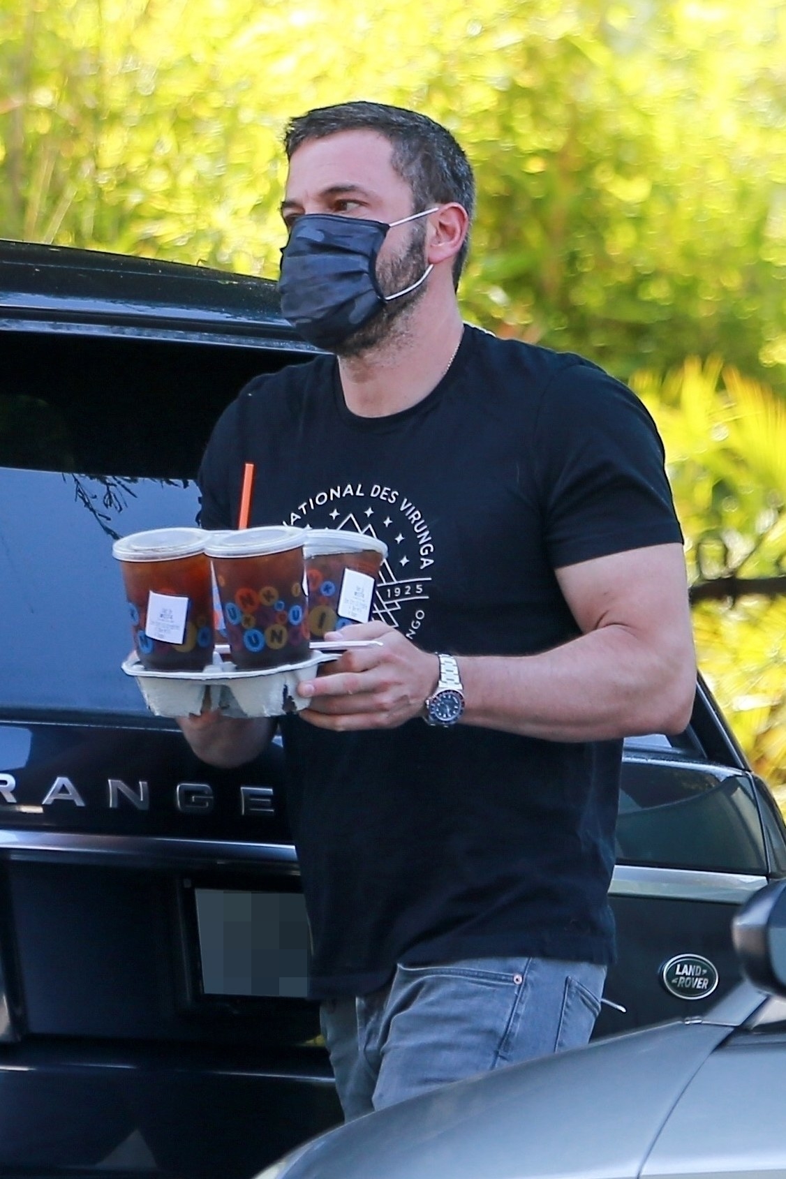 Ben walks, while wearing a face mask, and carries ice beverages in a to-go carrier